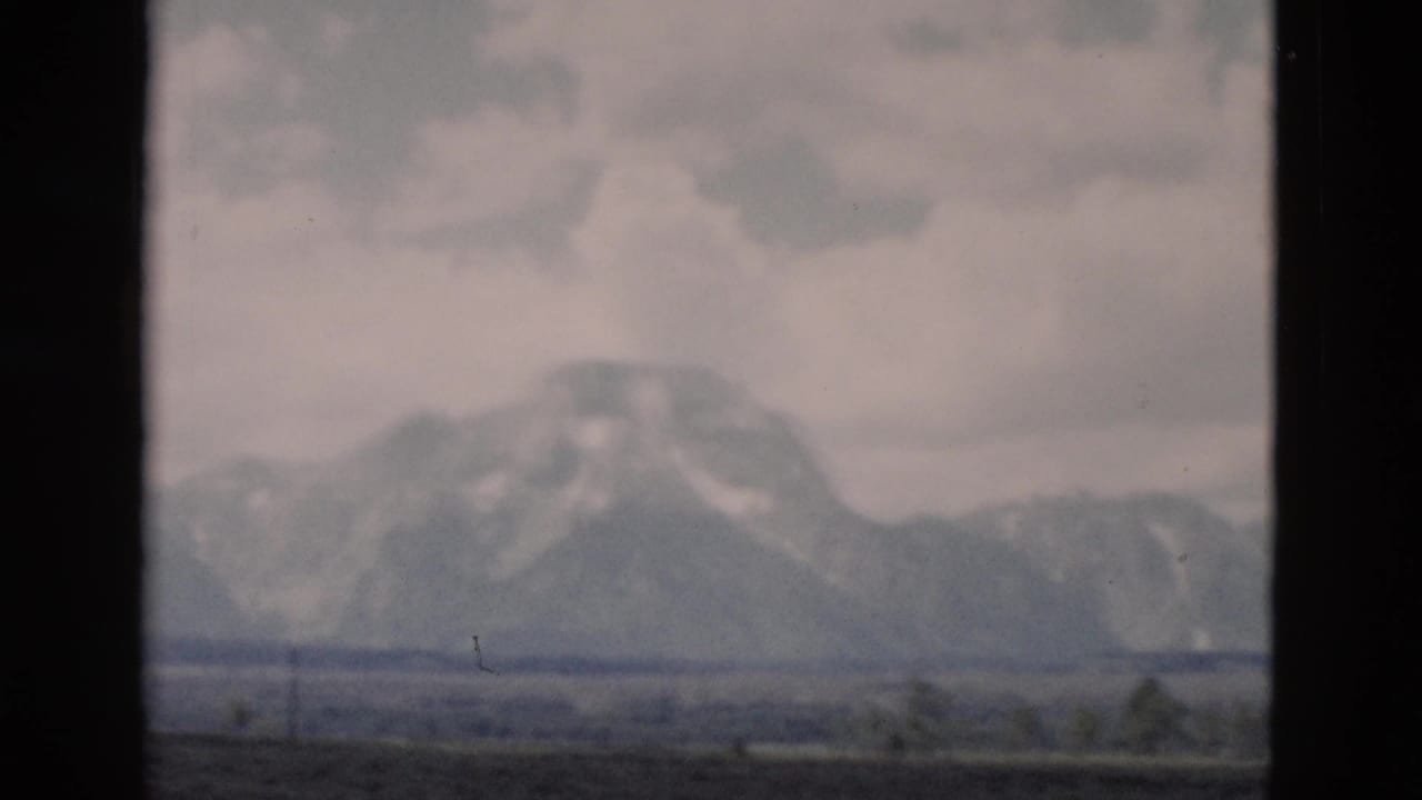 Distant snow-marked mountains under clouds, seen through dark vertical frame borders.
