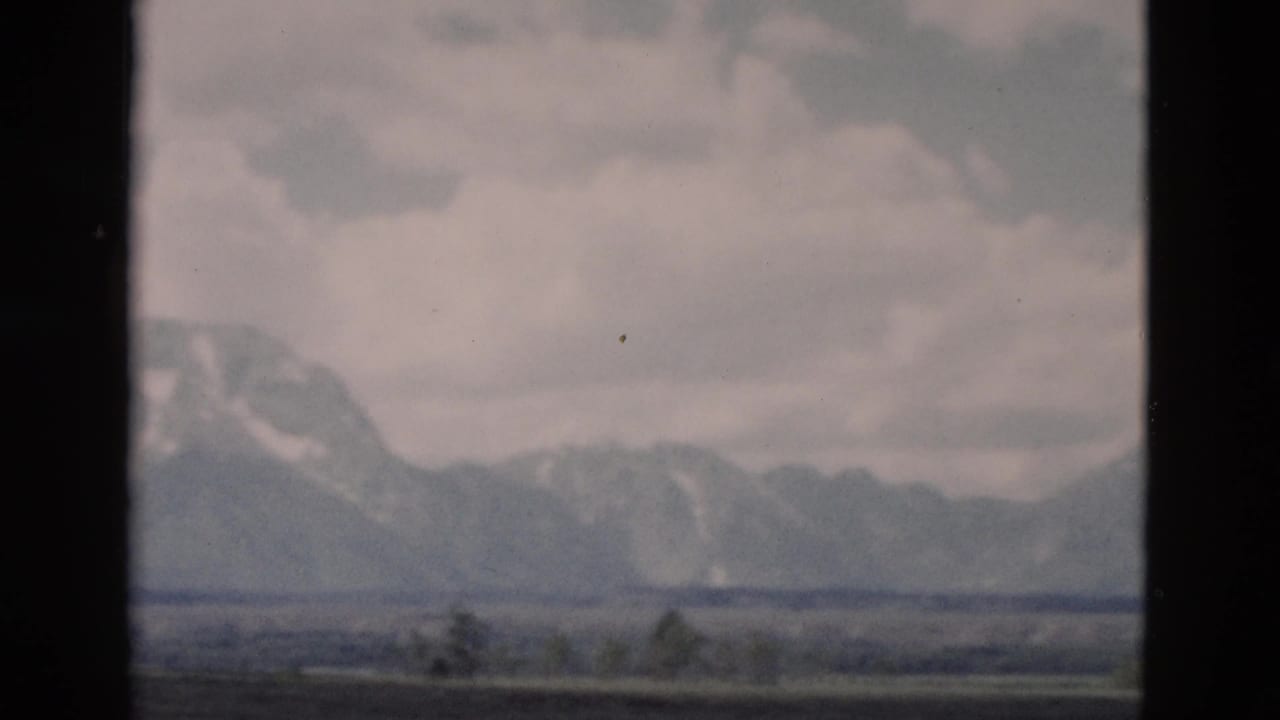 Distant Yellowstone mountain range appears through haze, with cloudy sky, muted color, and dark frame edges from the 8mm scan.