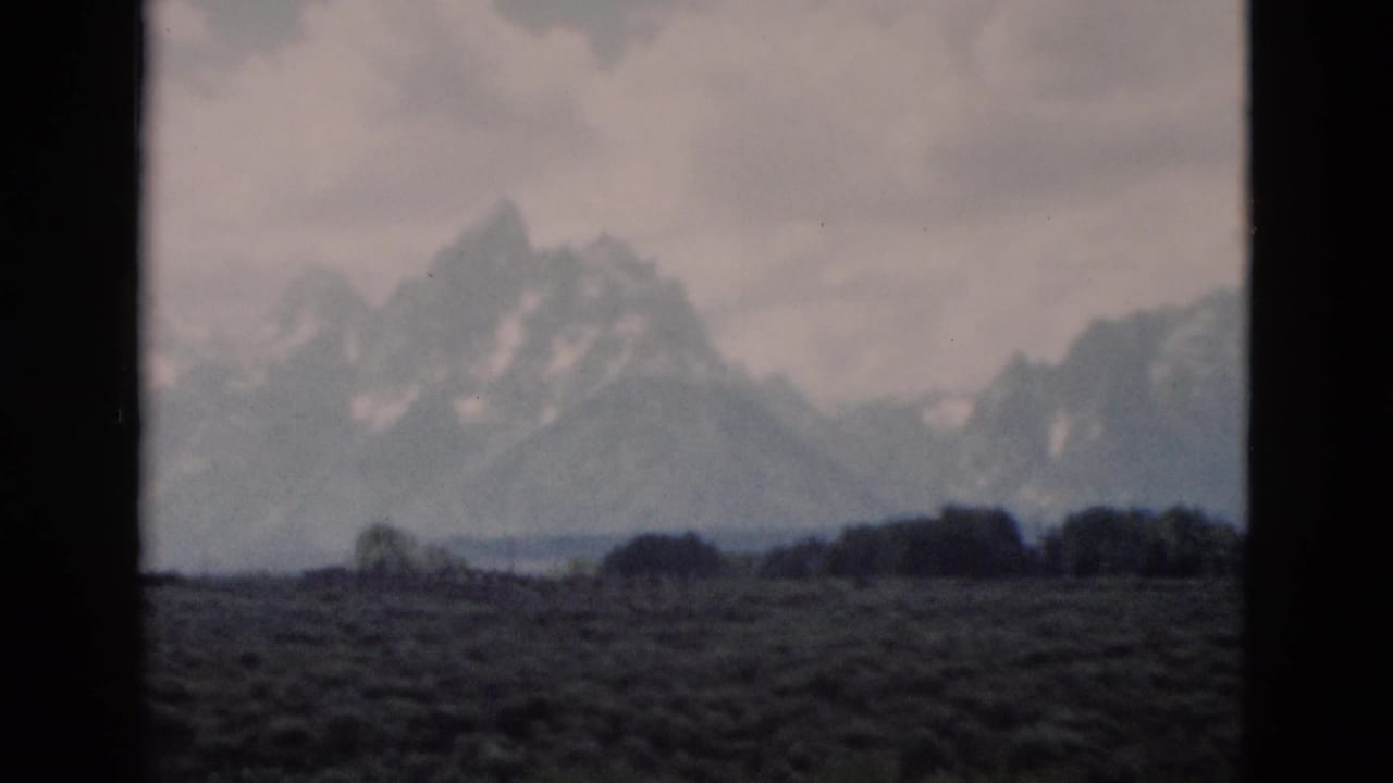Yellowstone, Wyoming mountain range seen across an open field in a soft, grainy 1958 8mm home-movie frame.