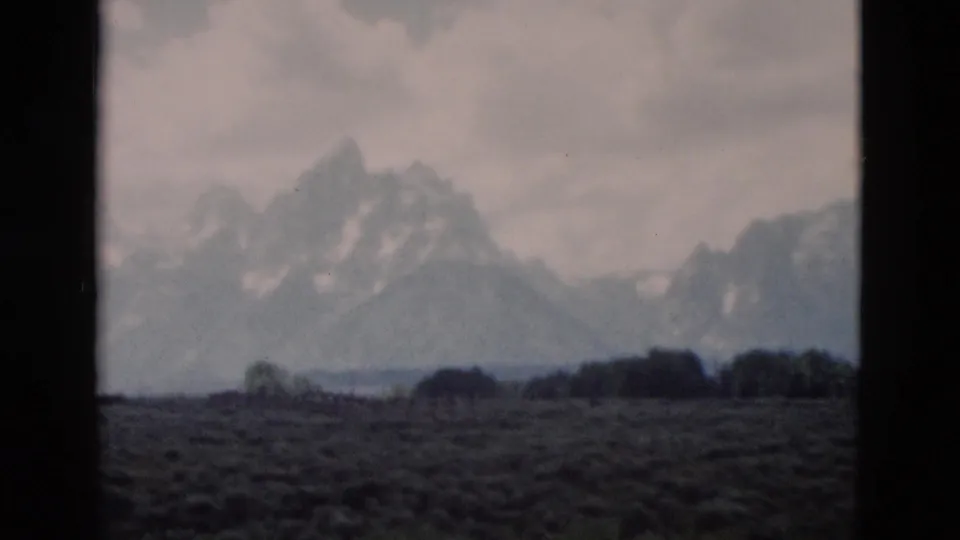 Yellowstone, Wyoming mountain range seen across an open field in a soft, grainy 1958 8mm home-movie frame.