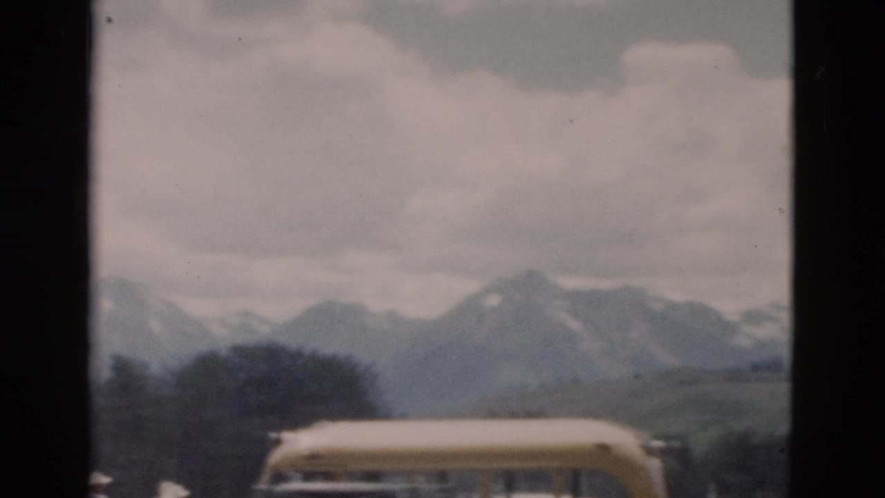 Yellow bus roof in foreground with mountains and clouds beyond.