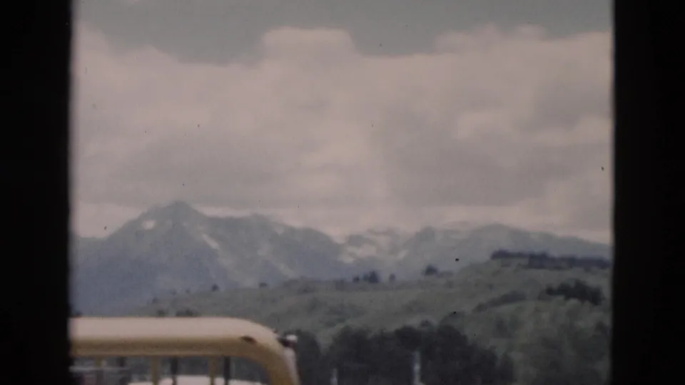 1958 visitor-shot frame with the corner of a yellow bus, open green hillside, and distant mountains in a western park landscape.