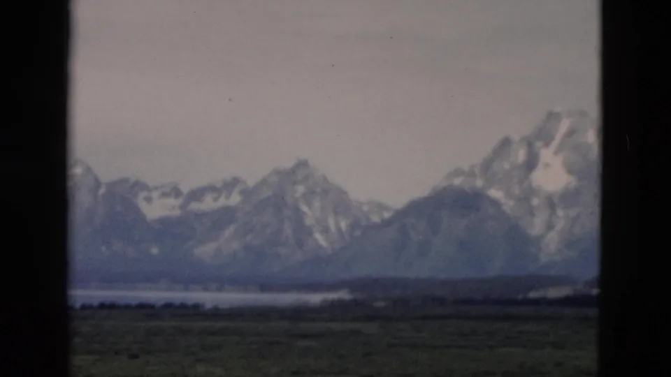 Scenic 8mm frame of a distant lake, dark foreground flats, and snow-capped mountains in the Yellowstone and Teton region.