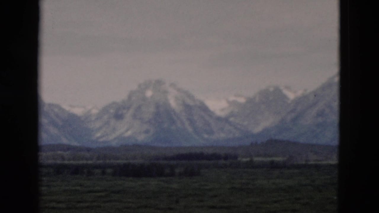 Snow-capped peaks and foothills appear in a soft 1958 8mm scenic view from the Yellowstone, Wyoming area.