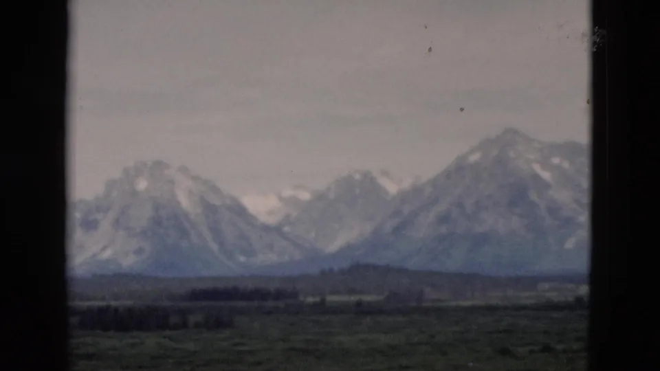 A vintage 8mm frame shows distant snow-streaked mountains and open foreground in the Yellowstone, Wyoming area.