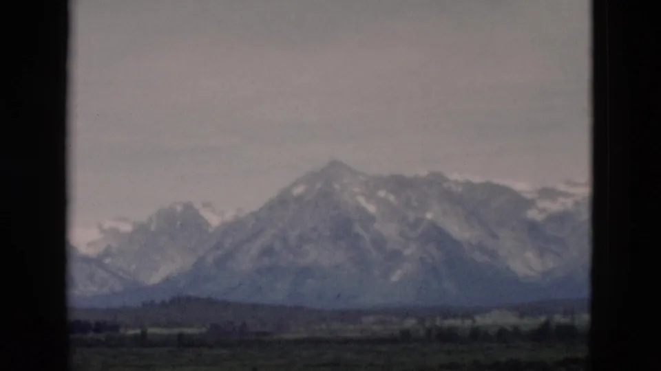 1958 8mm Yellowstone-area view of distant snowy mountains and valley framed by dark window edges.