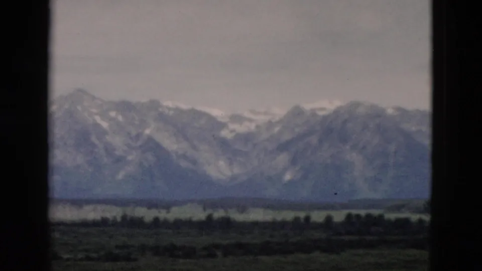 1958 Yellowstone-area home-movie view of mountain peaks, pale sky, and low valley vegetation framed by dark borders.
