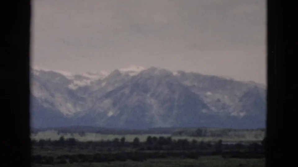 1958 Yellowstone-area 8mm frame with a mountain slope, muted valley greens, and soft haze across the sky.