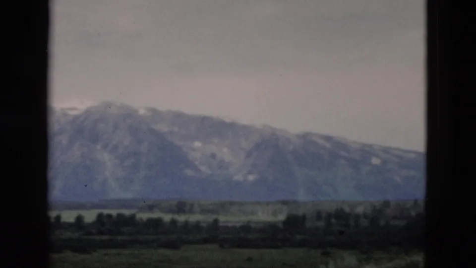 1958 Yellowstone-area home-movie frame showing a hazy mountain ridge beyond a green valley with scattered trees.