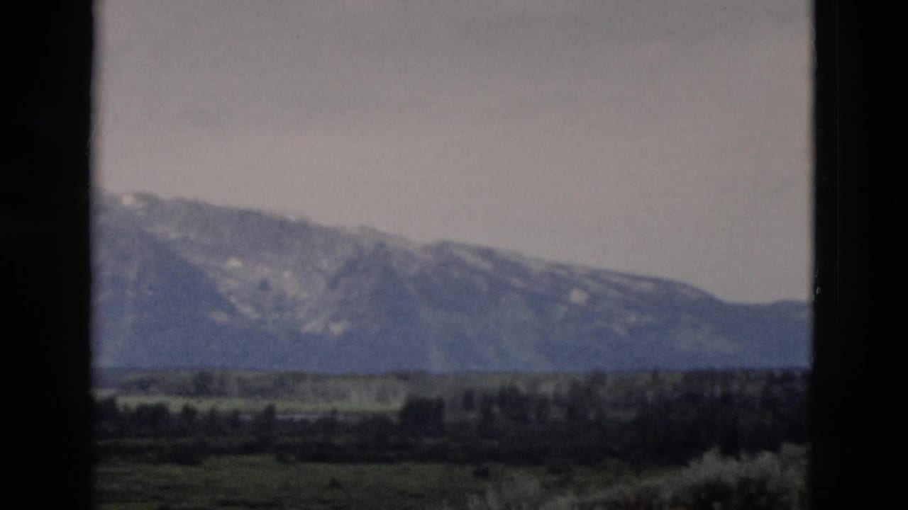 1958 8mm travel frame showing distant Yellowstone-area mountains across an open valley, seen through dark foreground edges.
