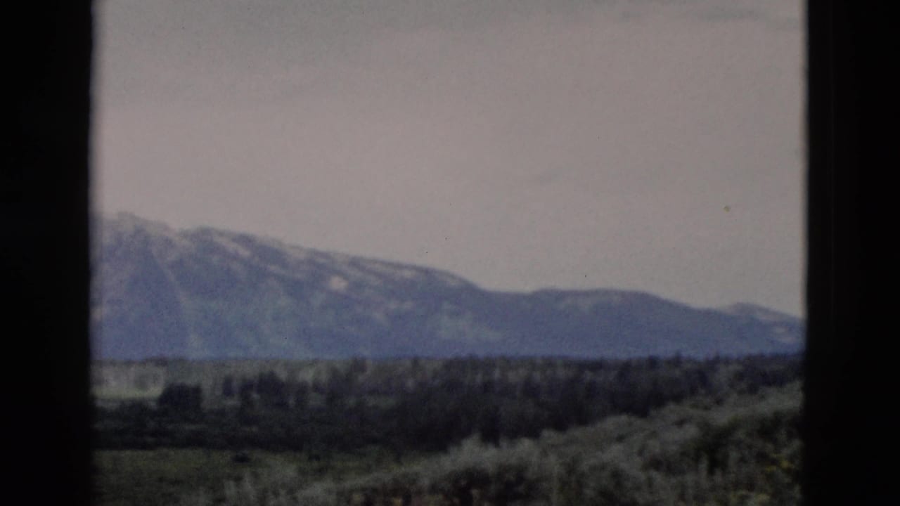 Mountain range and valley landscape framed by dark vertical film or window edges.