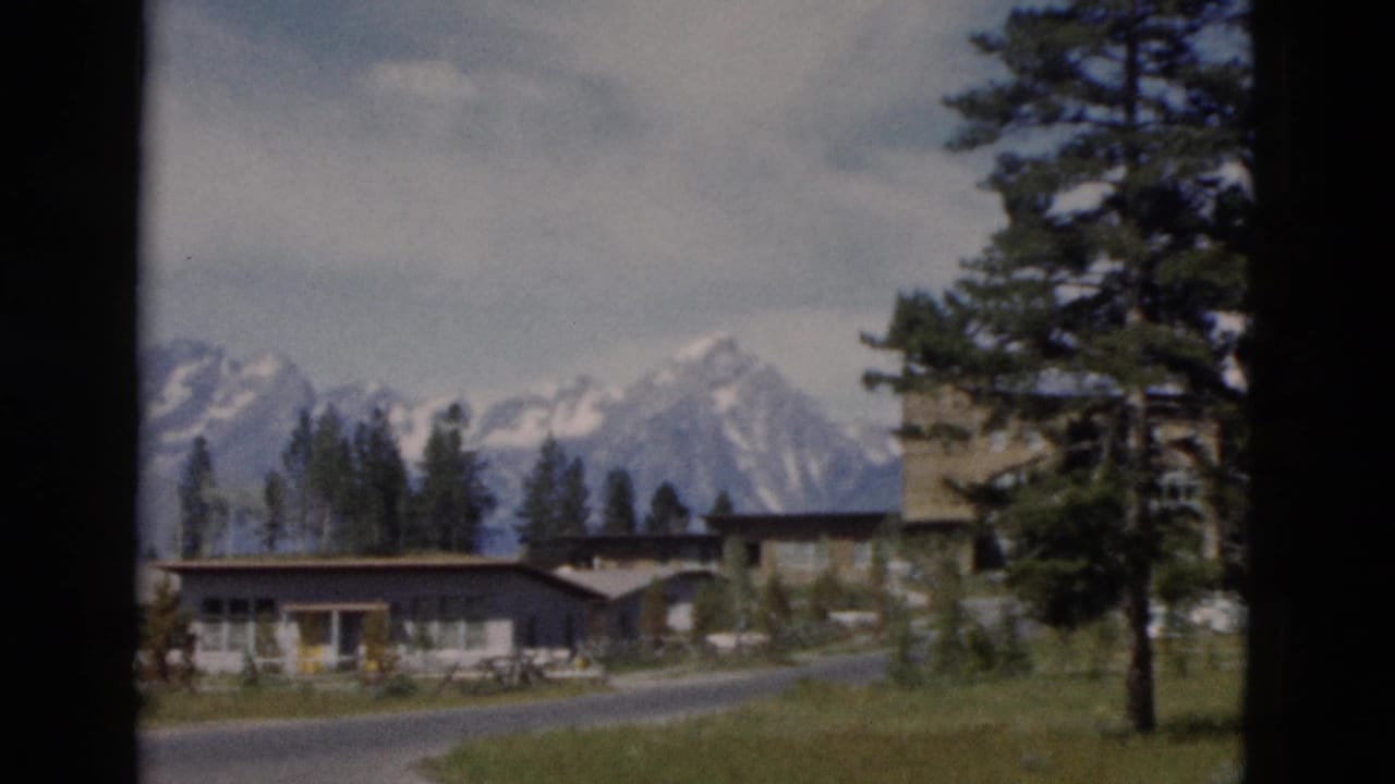 Yellowstone, Wyoming footage frame with lodge-like buildings, a curving road, pine trees, and distant snowy mountains.