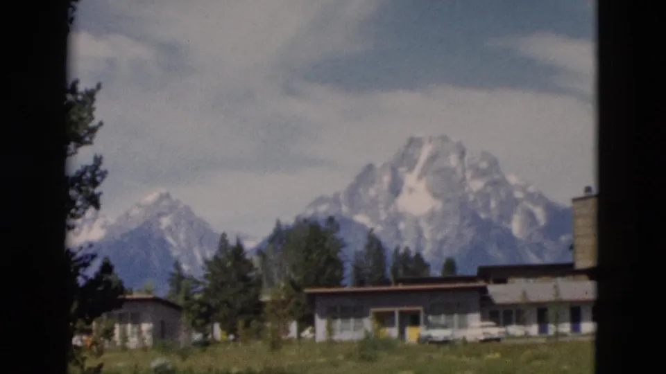 1958 8mm travel frame with low park-area buildings and trees in front of snow-capped Teton Range peaks.