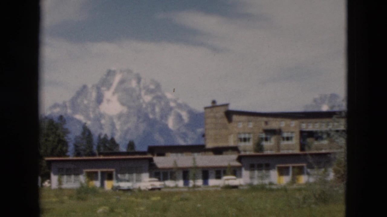 Low building complex with parked white cars and snow-capped mountains behind it.