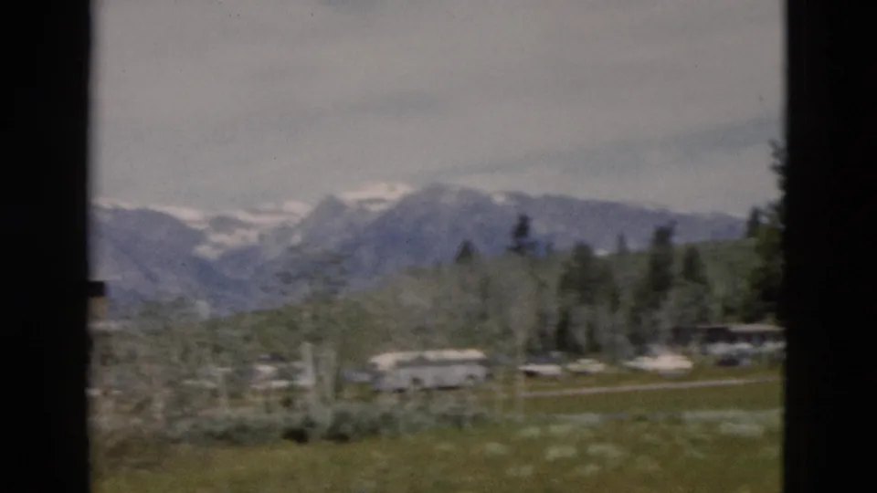 1958 Yellowstone-area 8mm frame with grass, pale trees, low visitor buildings, and mountains partly softened by motion.