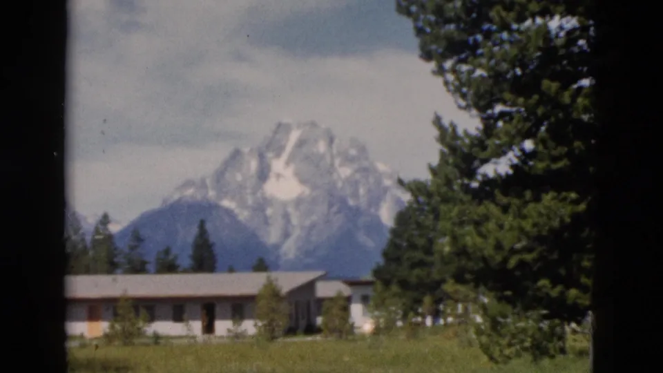1958 8mm Yellowstone-area frame with a low building and evergreens below the snow-capped Teton Range.