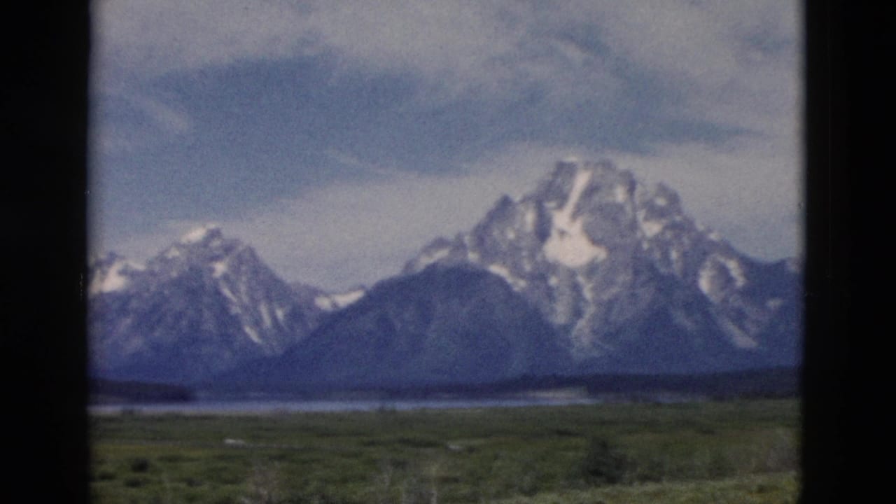 Snow-capped mountain range beyond a green valley, framed by dark 8mm film borders.