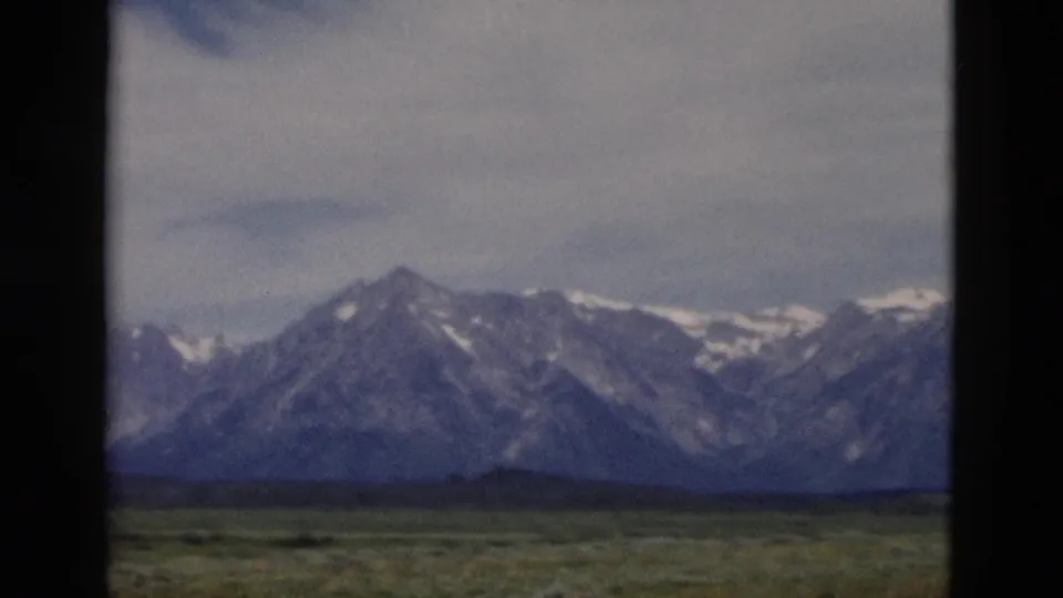 Vintage Yellowstone, Wyoming frame showing distant snow-capped mountains and open grassland in soft 8mm color.