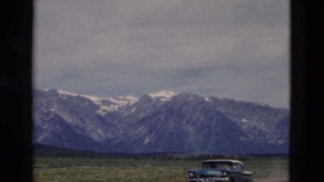 A rounded mid-century car crosses the foreground with Yellowstone-area mountains in the distance.