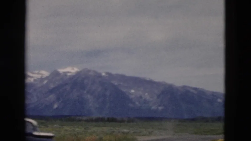 Soft 8mm frame of mountains, plains and a partial vehicle edge during a Wyoming road-view shot.