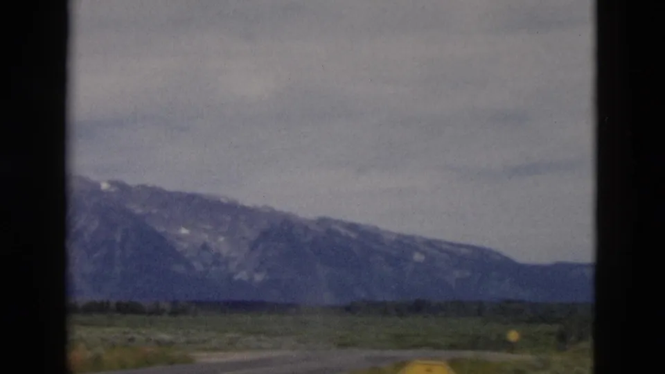 Roadside 8mm view of open Wyoming plains leading toward distant mountains near Yellowstone.