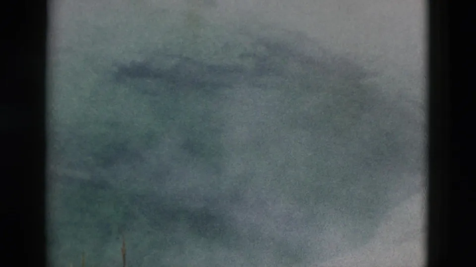 Soft, grainy 8mm view of vapor drifting across a partially frozen Yellowstone pond with sparse foreground grasses.