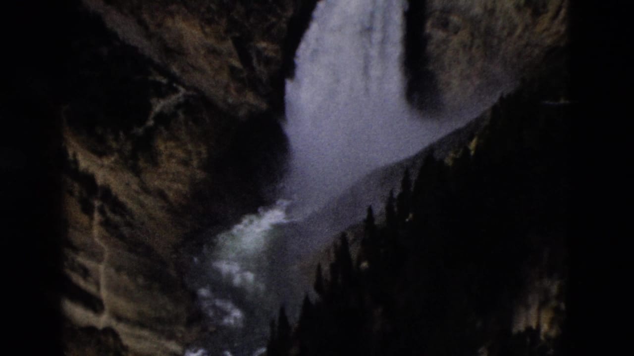 1958 8mm Yellowstone footage showing a white waterfall descending between rocky canyon walls and dark conifers.