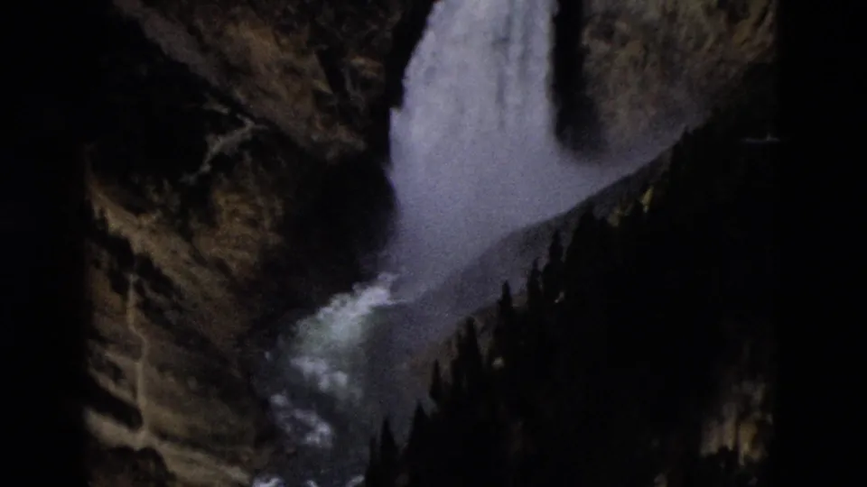 1958 8mm Yellowstone footage showing a white waterfall descending between rocky canyon walls and dark conifers.