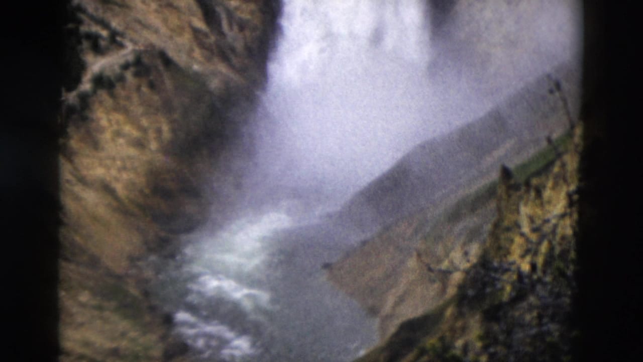 Yellowstone 8mm frame from 1958 showing waterfall spray, a river channel, and rugged canyon walls below the falls.