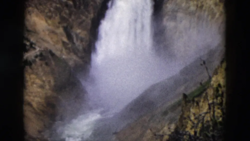 1958 Yellowstone home-movie frame with a closer view of the falls plunging into heavy mist beside canyon walls.