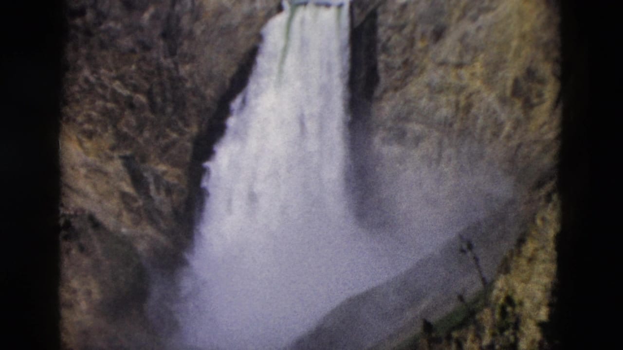 1958 Yellowstone home-movie frame showing a waterfall plunging through a rocky canyon with mist near the base.