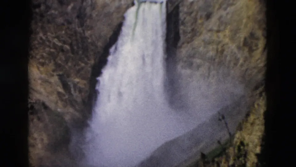 1958 Yellowstone home-movie frame showing a waterfall plunging through a rocky canyon with mist near the base.