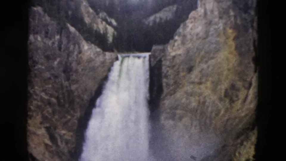 1958 Yellowstone frame with the waterfall lower in view, revealing more canyon wall and forested terrain above.