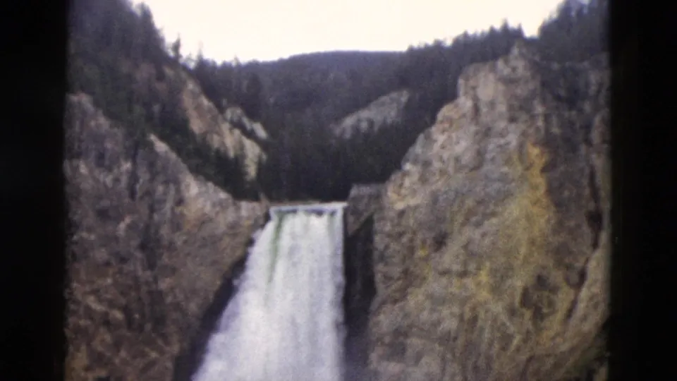 Yellowstone waterfall in a wider 1958 home-movie view, with canyon walls, ridge trees, and mist around the plunge.