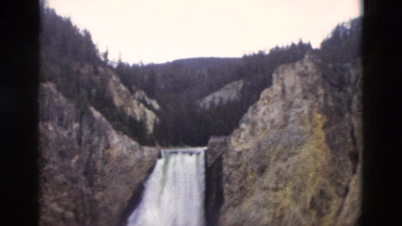 Waterfall drops through a rocky canyon below forested ridges.