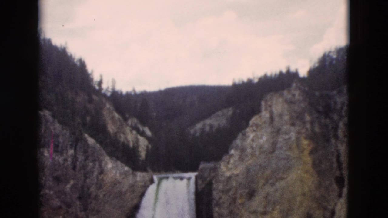Yellowstone, Wyoming 8mm frame with a distant waterfall, rugged canyon rock, and pine forest along the ridge.