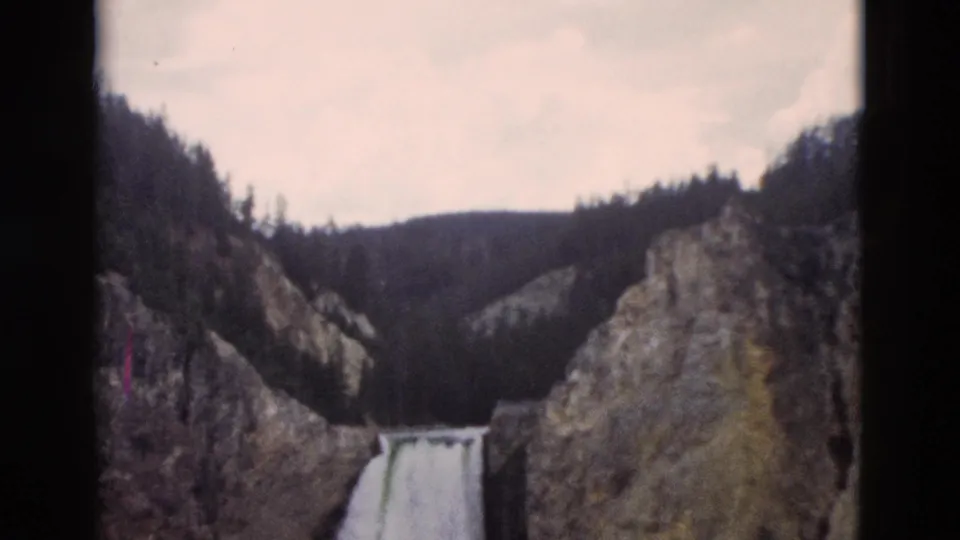 Yellowstone, Wyoming 8mm frame with a distant waterfall, rugged canyon rock, and pine forest along the ridge.