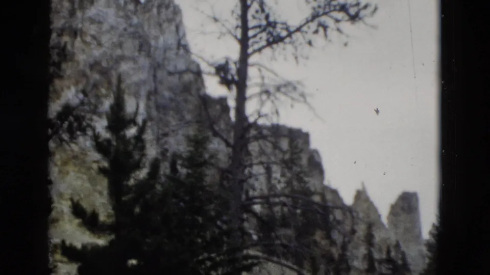 1958 Yellowstone 8mm frame with rugged cliffs, conifers, bare branches, and heavy dark framing from the film scan.