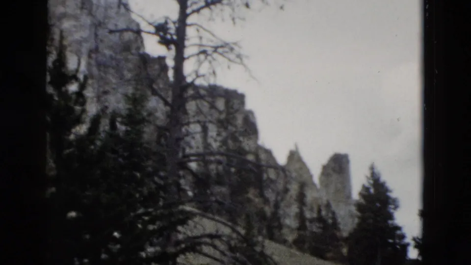 1958 Yellowstone 8mm frame showing pointed rock formations, tree silhouettes, pale sky, and faded home-movie color.