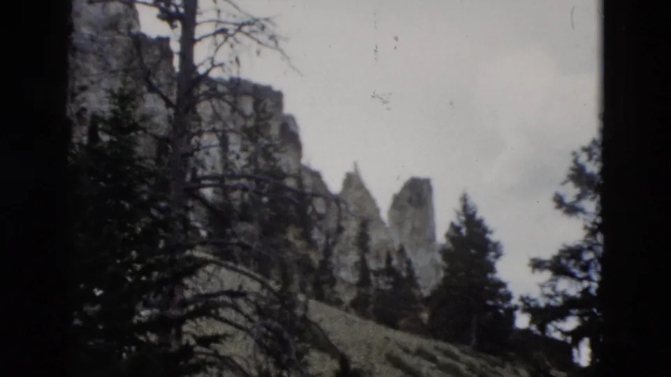 1958 Yellowstone 8mm frame with rock spires, evergreen trees, bare branches, and visible film grain at the pan's end.