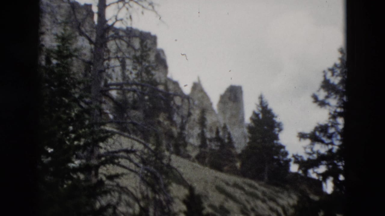 1958 Yellowstone home-movie view of rocky canyon formations, dark trees, and a sloping meadow seen through soft 8mm film exposure.