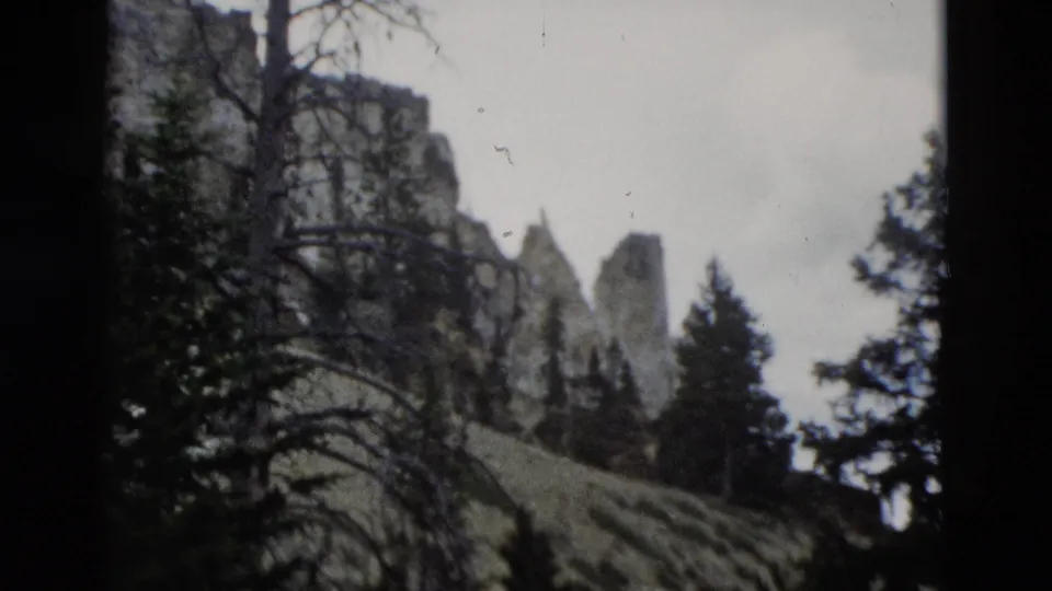 1958 Yellowstone home-movie view of rocky canyon formations, dark trees, and a sloping meadow seen through soft 8mm film exposure.