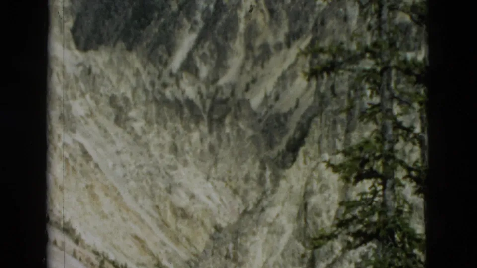 1958 Yellowstone frame with softened exposure showing steep canyon walls, scattered pines, and a river bend partly hidden by framing and distance.