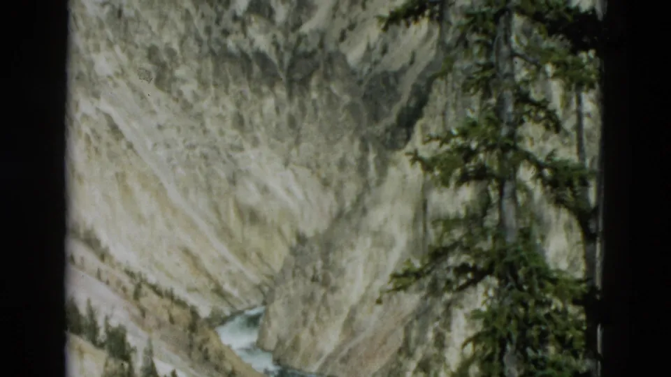 1958 Yellowstone 8mm frame showing the river below a steep canyon, with pale rock faces and dense evergreen branches at the right edge.