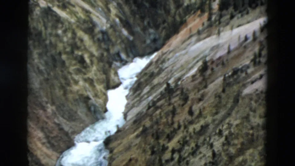 1958 Yellowstone home-movie frame of white water below layered canyon cliffs, with an evergreen at the right edge.