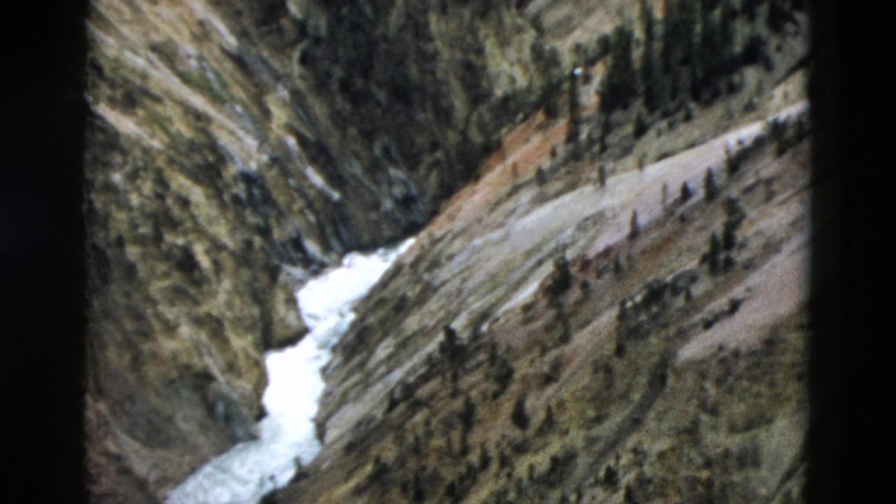 Rocky canyon slope with white snowmelt and scattered conifer trees.