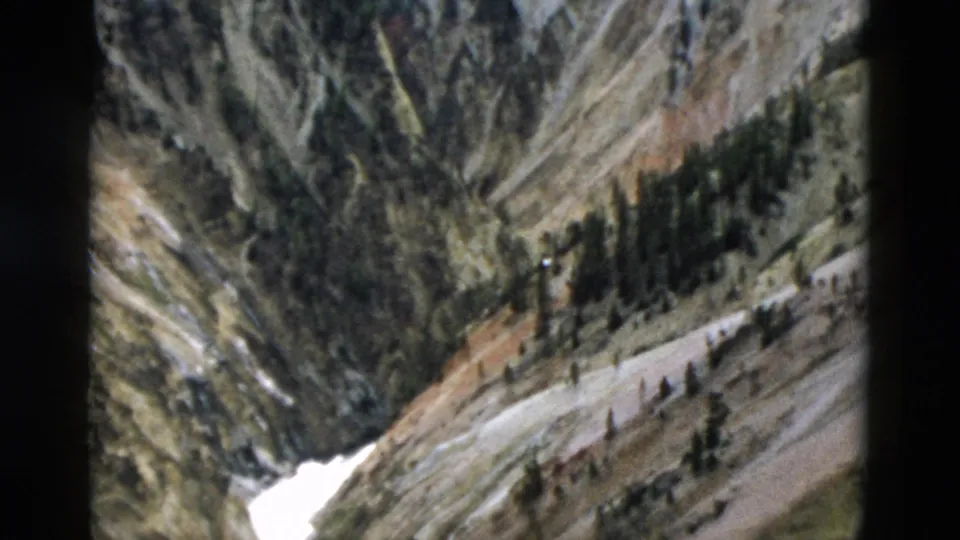 1958 Yellowstone landscape frame showing bright melting snow below a rocky slope with conifers and pale exposed ground.