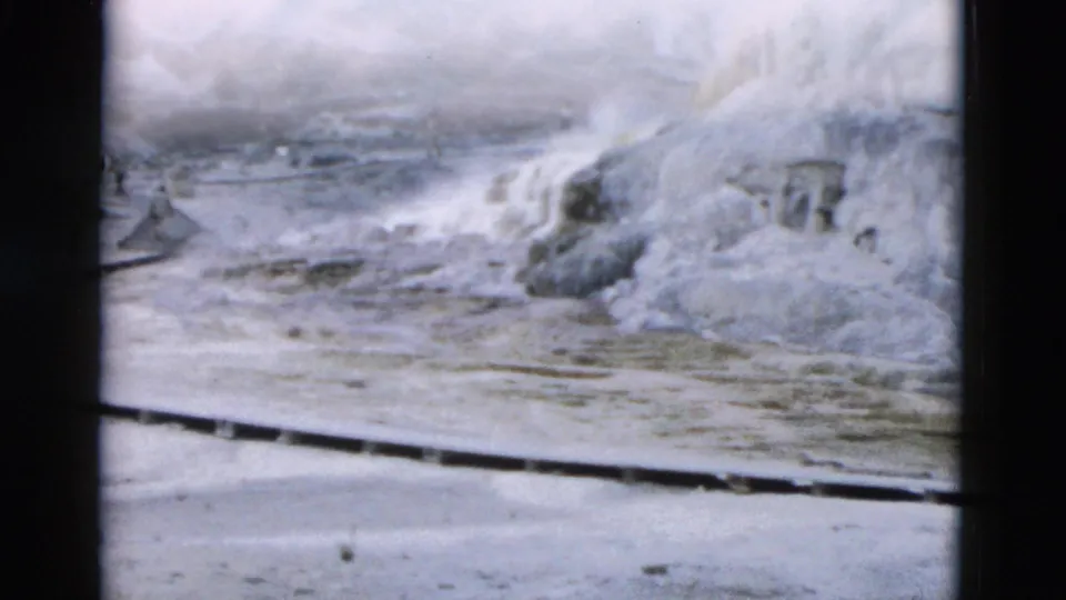 1958 Yellowstone home-movie frame showing pale mineral terraces, runoff, and hazy geothermal ground.