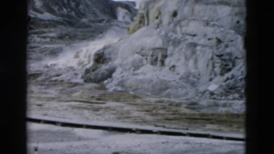 1958 Yellowstone frame showing pale geothermal formations, shallow runoff, and textured mineral surfaces.