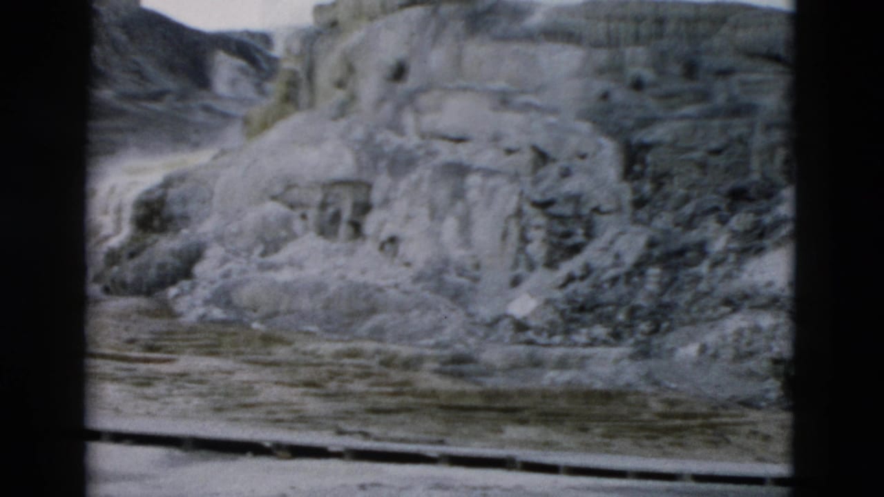 Yellowstone home-movie still showing layered pale terrace formations and a flat wet foreground, with soft 8mm color and grain.